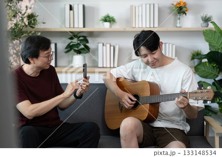 Father capturing son playing guitar, sharing musical moments Father capturing son playing guitar, sharing musical moments 133148534