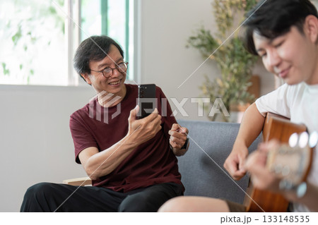 Father enjoying son guitar performance, capturing joyful moments 133148535