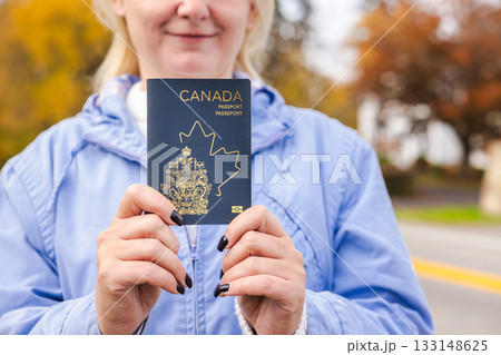 Woman outdoors holding a Canadian passport with both hands, showing the cover close to the camera during an autumn day. 133148625