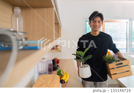 Home Gardening. Young man carrying plants and flowers in his living space. Home Gardening. Young man carrying plants and flowers in his living space. 133148719