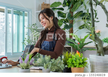 Sustainable Gardening. Smiling woman in apron engaging with customers in a plant shop. Sustainable Gardening. Smiling woman in apron engaging with customers in a plant shop. 133148819