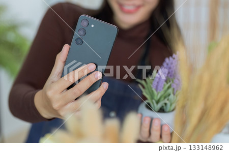 Sustainability. Woman taking selfie with smartphone and potted lavender plant indoors. 133148962