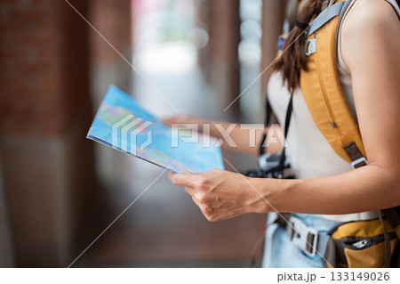 Travel. Young woman reading map while exploring city streets. 133149026