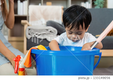 Curious Child. A toddler exploring a bucket of cleaning supplies with his mother nearby. 133149056