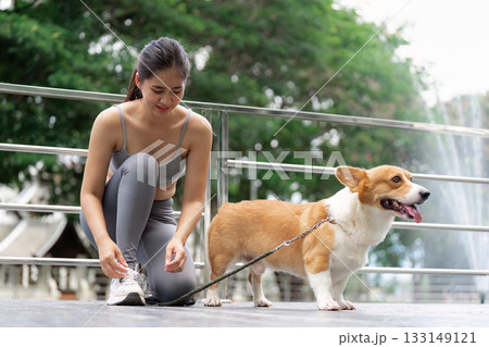 Wellness and Fitness. Young woman tying shoelaces next to her corgi before a walk. Wellness and Fitness. Young woman tying shoelaces next to her corgi before a walk. 133149121