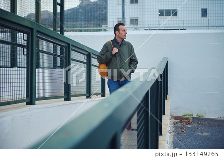 Man With Orange Backpack Walking Along Green Railing In Urban Setting Man With Orange Backpack Walking Along Green Railing In Urban Setting 133149265