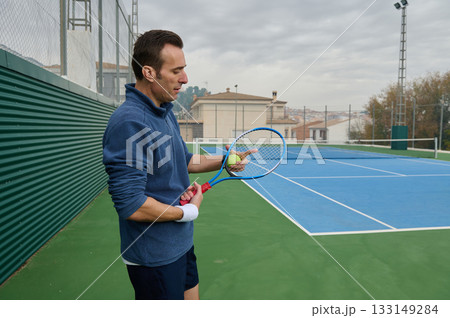 Focused Man Preparing Tennis Serve On Outdoor Blue Court With Racket And Ball 133149284