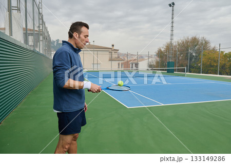 Focused Tennis Player Practicing on Outdoor Court with Racket and Ball 133149286