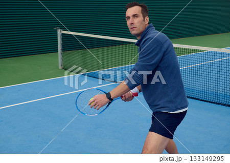 Focused Tennis Player on Blue Court Preparing to Serve with Ball and Racket 133149295