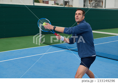 Focused Tennis Player In Blue Long-Sleeve Shirt Aiming Serve On Outdoor Court 133149296
