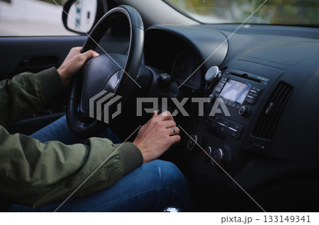 Driver With Hands On Steering Wheel In Car Interior, Focused On Driving Controls Driver With Hands On Steering Wheel In Car Interior, Focused On Driving Controls 133149341