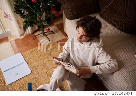 Teen Boy Reading Book At Home By Christmas Tree In Cozy Living Room Christmas Mood 133149471