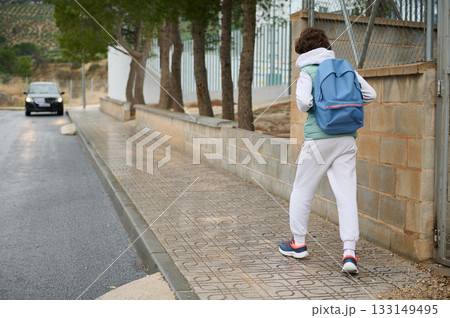 Teenager With Blue Backpack Walking Along Sidewalk On Suburban Street Teenager With Blue Backpack Walking Along Sidewalk On Suburban Street 133149495