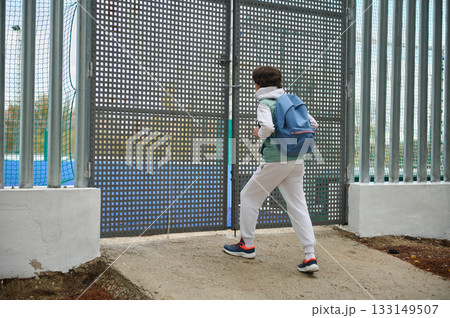 Teenager With Backpack Approaches Industrial Gate in Outdoor Fenced Area 133149507
