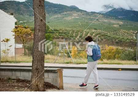 Teen Boy With Backpack Walking Along Suburban Street With Hills In The Distance 133149529