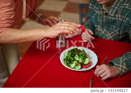 Teenage Friends Sharing Salad at Red Table While Salt Is Shaken Onto Plate Teenage Friends Sharing Salad at Red Table While Salt Is Shaken Onto Plate 133149817