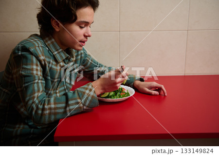 Teen Boy Eating Salad At A Red Table In A Quiet Kitchen Setting Teen Boy Eating Salad At A Red Table In A Quiet Kitchen Setting 133149824