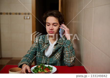 Teenager Talks On Phone At Diner Table With Salad, Casual Plaid Shirt, Quiet Everyday Moment Teenager Talks On Phone At Diner Table With Salad, Casual Plaid Shirt, Quiet Everyday Moment 133149842