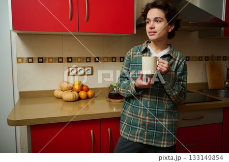 Teenager In A Modern Kitchen Holds A Coffee Mug, Reflecting A Quiet Fall Morning Teenager In A Modern Kitchen Holds A Coffee Mug, Reflecting A Quiet Fall Morning 133149854