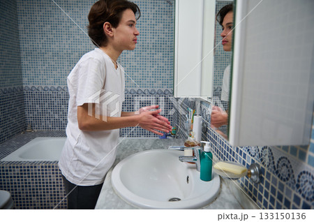 Teen Boy Washing Hands at Bathroom Sink with Mirror in Blue Tile Room Teen Boy Washing Hands at Bathroom Sink with Mirror in Blue Tile Room 133150136