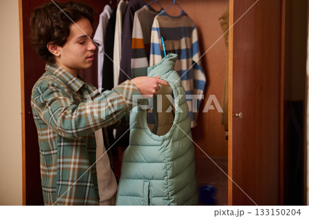 Teenage Boy Trying On Light Blue Puffer Vest In Closet For Style Check 133150204