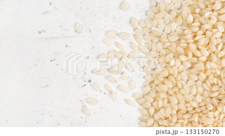 White sesame - Sesamum indicum - seeds on white stone like board, view from above, space for text left side White sesame - Sesamum indicum - seeds on white stone like board, view from above, space for text left side 133150270