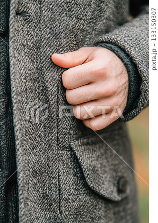 Textured herringbone overcoat detail with wood button and human hand gesture. 133150307
