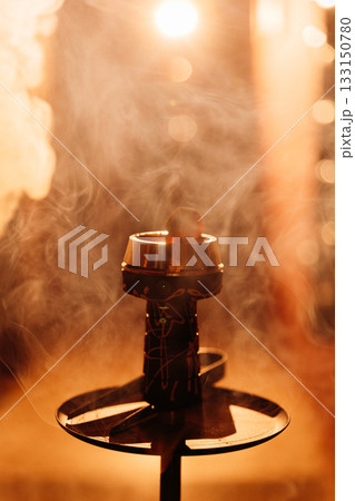 Hookah bowl with glowing coal and drifting smoke in warm bokeh bar light Hookah bowl with glowing coal and drifting smoke in warm bokeh bar light 133150780