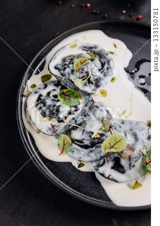 Black ravioli in creamy white sauce with microgreens, gourmet plating on dark slate 133150781