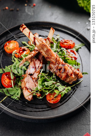 Grilled ribs on arugula with cherry tomatoes and balsamic glaze, restaurant plating 133150785