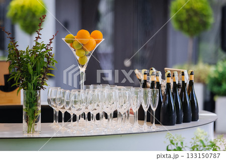 Outdoor champagne bar with citrus centerpiece, glass flutes and bottles ready for service 133150787