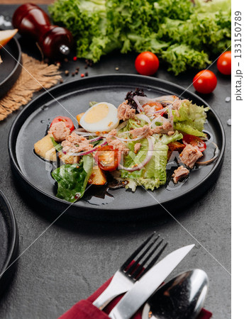 Tuna salad with egg, tomatoes and greens on black plate, restaurant lunch closeup 133150789