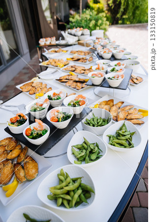 Catering buffet with edamame bowls, shrimp salads, and baked mussels outdoors 133150819