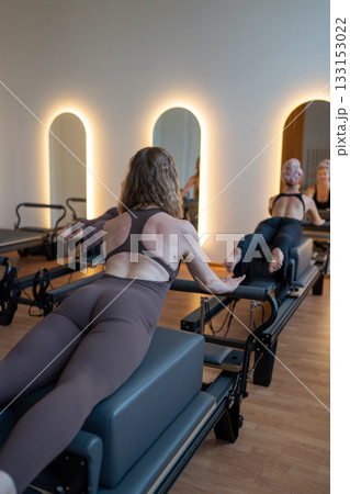 Group of caucasian women exercising with trainer on pilates reformers in a bright studio. Their workout focuses on core strength and flexibility in a modern fitness environment 133153022