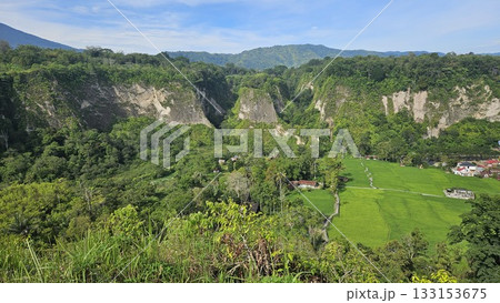 A stunning viewpoint at Panorama Ngarai Sianok showcases lush greenery, towering trees, and a majestic mountain under the clear blue sky, offering a peaceful harmony. A stunning viewpoint at Panorama Ngarai Sianok showcases lush greenery, towering trees, and a majestic mountain under the clear blue sky, offering a peaceful harmony. 133153675