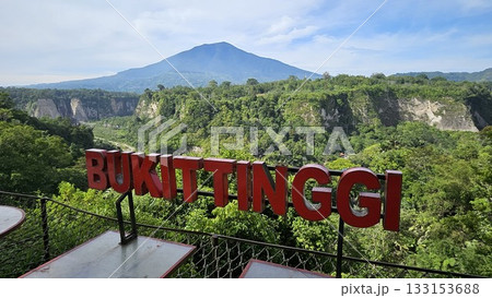 A stunning viewpoint at Panorama Ngarai Sianok showcases lush greenery, towering trees, and a majestic mountain under the clear blue sky, offering a peaceful harmony. 133153688