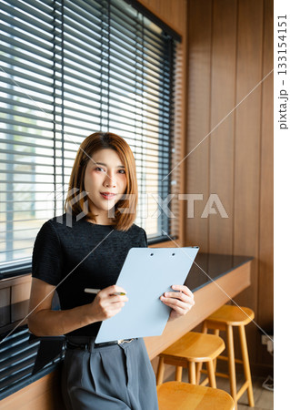 Asian businesswoman in a modern office gives a thumbs-up while holding a clipboard. A confident portrait symbolizing professional success Asian businesswoman in a modern office gives a thumbs-up while holding a clipboard. A confident portrait symbolizing professional success 133154151