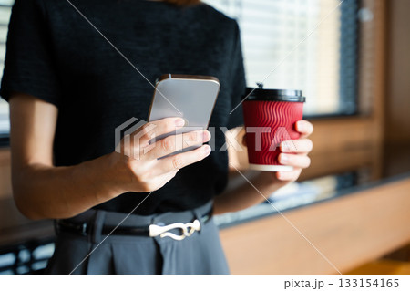 Asian businesswoman holds smartphone and coffee cup in a modern office, showcasing multitasking, digital connectivity Asian businesswoman holds smartphone and coffee cup in a modern office, showcasing multitasking, digital connectivity 133154165
