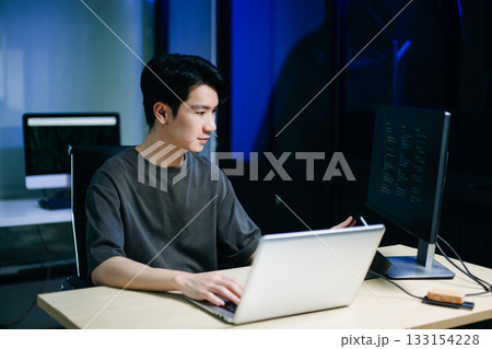 Young male programmer working with tablet and screen displaying code. Modern tech office setup, great for software, coding, IT 133154228