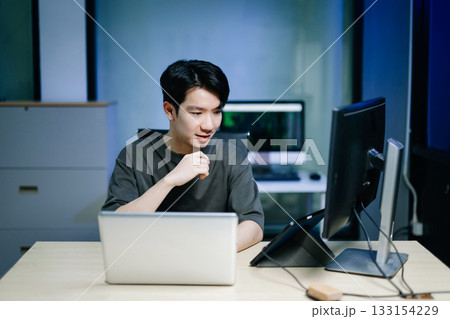 Young male programmer working with tablet and screen displaying code. Modern tech office setup, great for software, coding, IT 133154229