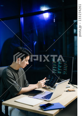 Young male programmer working with tablet and screen displaying code. Modern tech office setup, great for software, coding, IT 133154261