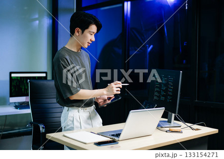 Asian developer writing code at night in modern office setup. Concept of software engineering, programming, digital workspace 133154271