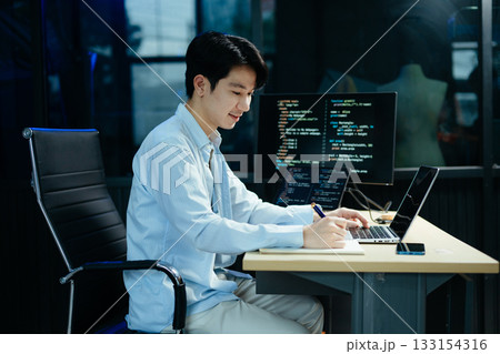 Young male programmer working with tablet and screen displaying code. Modern tech office setup, great for software 133154316