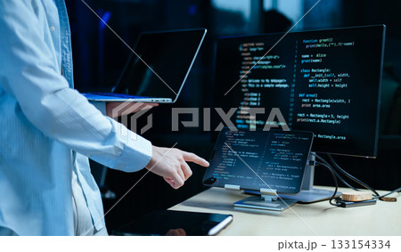 Young male programmer working with tablet and screen displaying code. Modern tech office setup, great for software 133154334