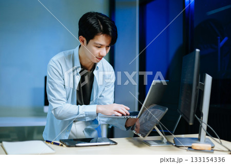 Young male programmer working with tablet and screen displaying code. Modern tech office setup, great for software 133154336