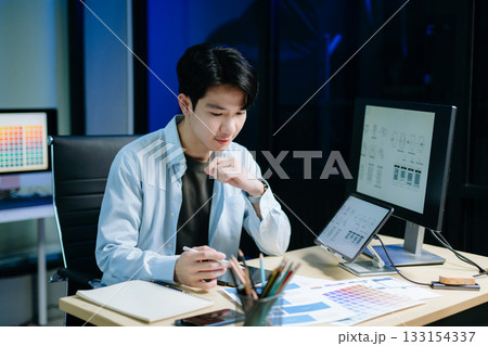 Asian male designer pointing at UX wireframes on screen and tablet in modern office. Ideal for themes in UI UX, digital product design, software 133154337