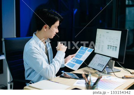 Asian male designer pointing at UX wireframes on screen and tablet in modern office. Ideal for themes in UI UX, digital product design, software 133154342