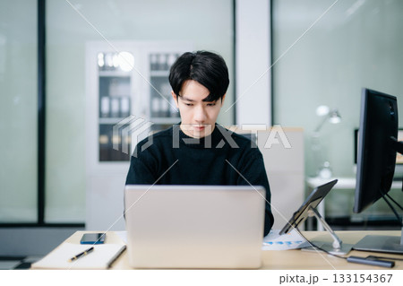 Asian man using laptop and tablet while sitting at her working place. Concentrated at work. 133154367