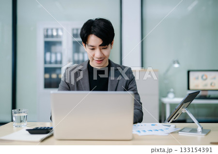 Confident young Asian businessman analyzing financial charts on laptop. Perfect for stock themes in business, finance Confident young Asian businessman analyzing financial charts on laptop. Perfect for stock themes in business, finance 133154391