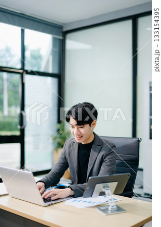 Confident young Asian businessman analyzing financial charts on laptop. Perfect for stock themes in business, finance Confident young Asian businessman analyzing financial charts on laptop. Perfect for stock themes in business, finance 133154395